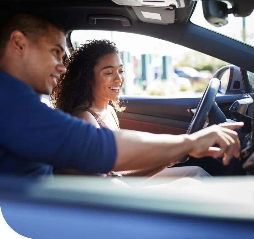 A young male and female couple sit together inside of a car.