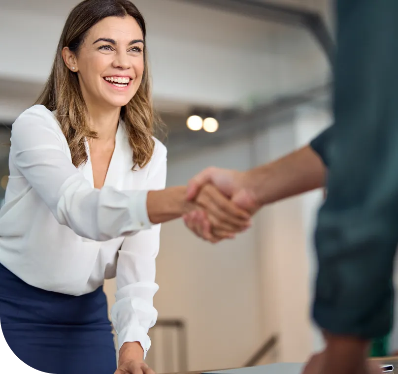 A smiling business woman shakes hands with a colleague in an office