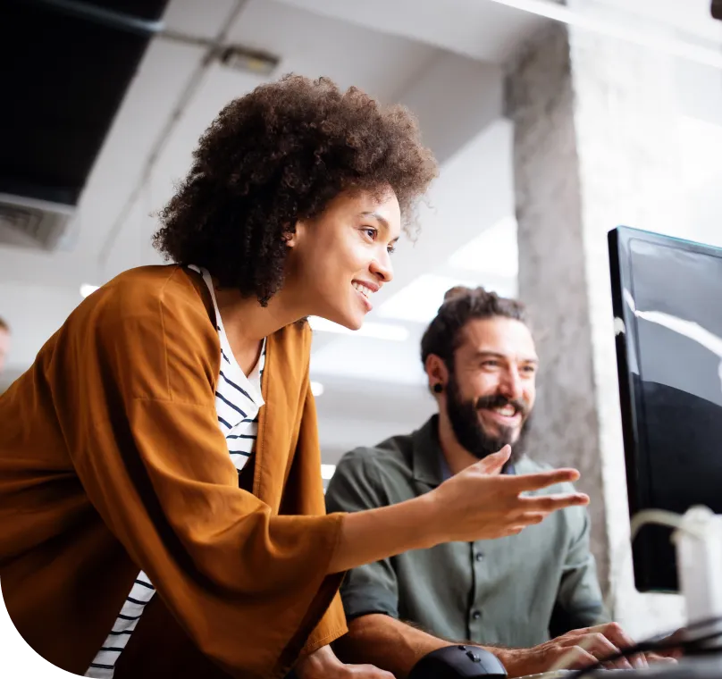 A smiling man and smiling woman work confidently in an office on a desktop computer
