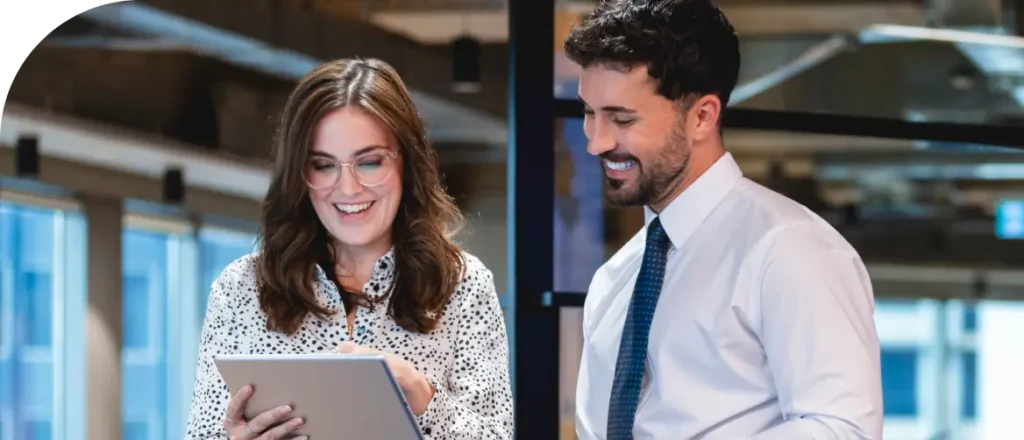 A man and woman collaborate in an office setting using a digital tablet.