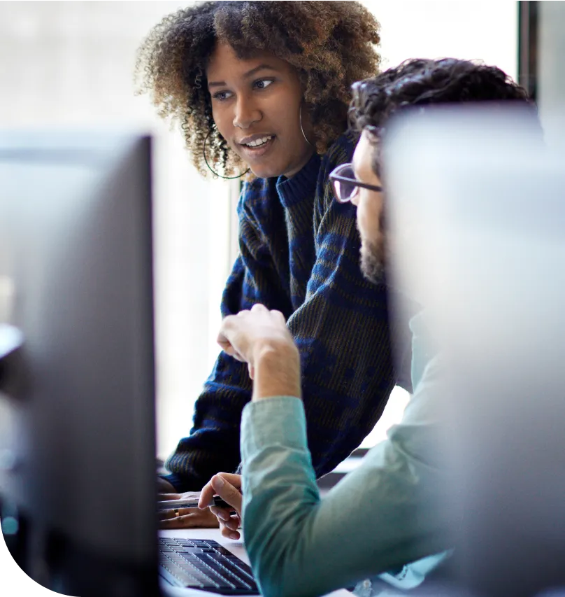 Two colleagues work together and use a desktop computer in an office setting