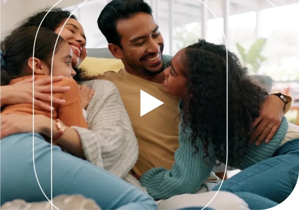 Video thumbnail of a family for four (mother, father, and two daughters) sit on the couch, smiling
