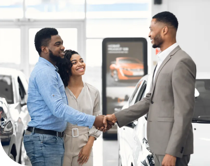 A couple shake hands with a salesman at a car dealership
