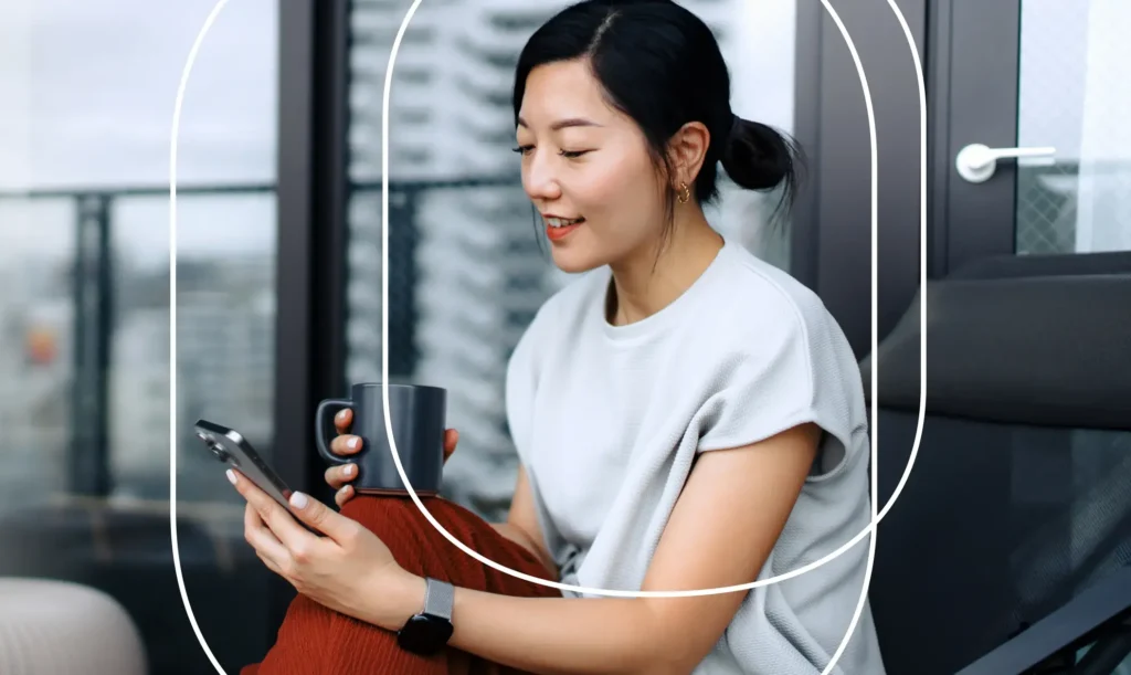 A woman sits on a balcony while viewing a mobile phone screen