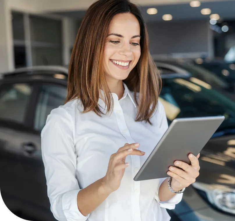 A female car salesperson views a tablet computer in a dealership showroom