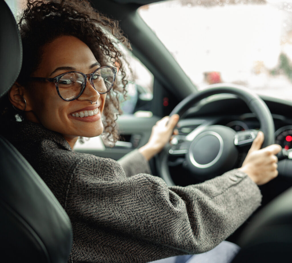 A smiling woman sits in the driver's seat of a car