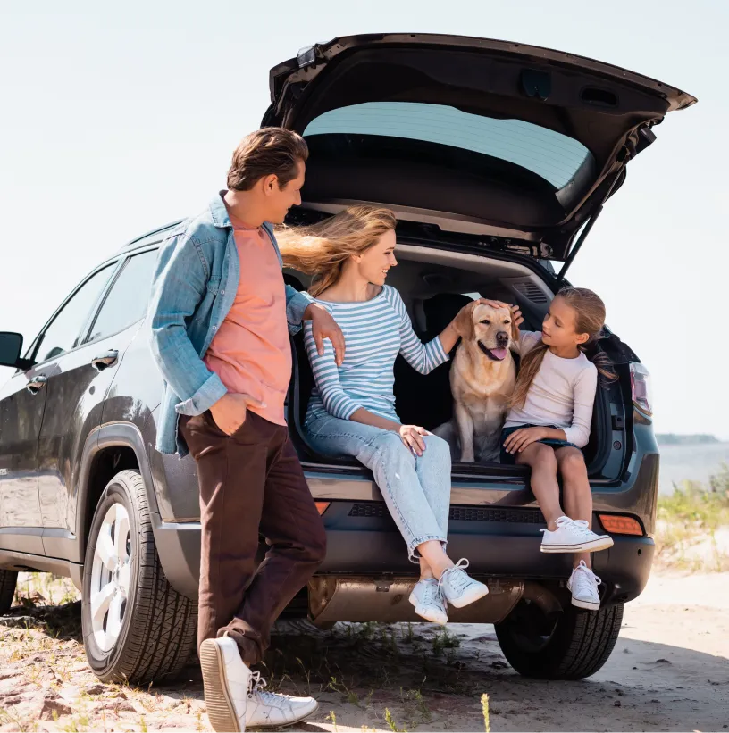 A family sit in the back of their SUV with their dog