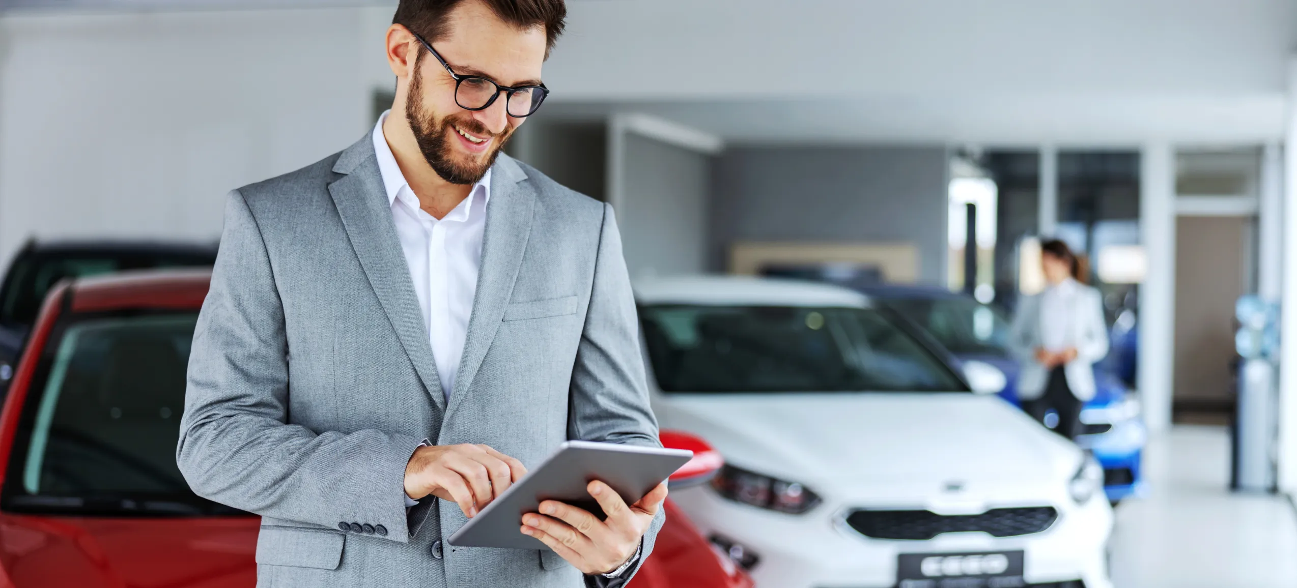 A dealer salesman looks at a digital tablet inside of a dealership showroom