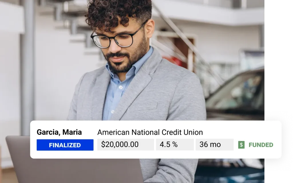 A salesman looks at a computer screen inside of a dealership showroom. A UI element featuring customer loan information is overlaid on the photo.