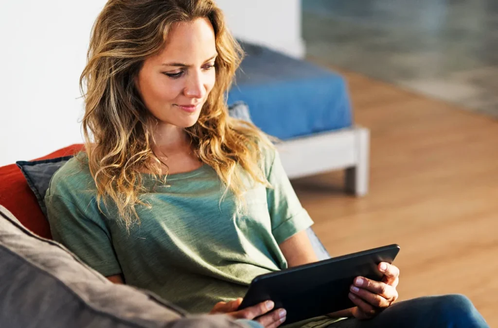 A woman uses a digital tablet while sitting at home on her couch